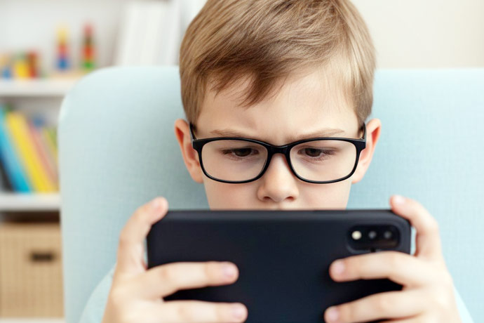 Un copil cu ochelari care se uita pe smartphone - Afla cum poti controla miopia si progresia ei.